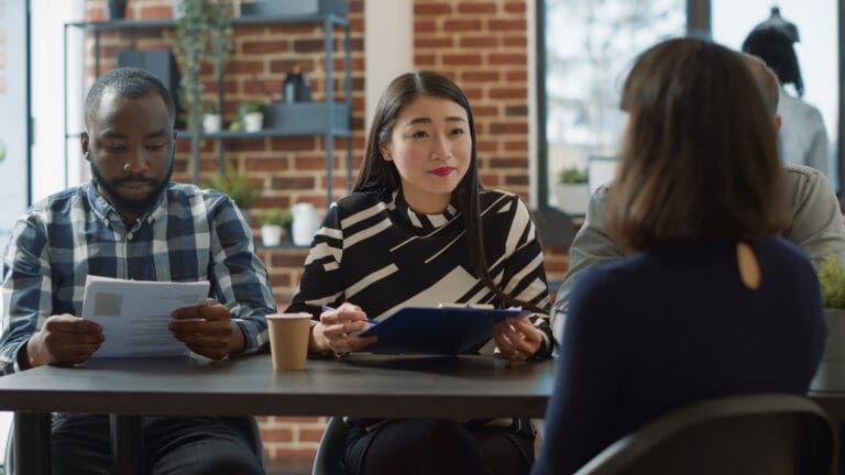 Diverse hiring panel interviewing a candidate in a modern office setting, reviewing resumes and making fair hiring decisions.